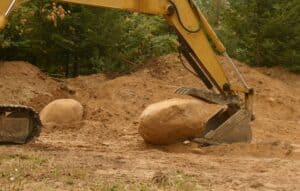 trackhoe bucket scooping up large heavy boulder